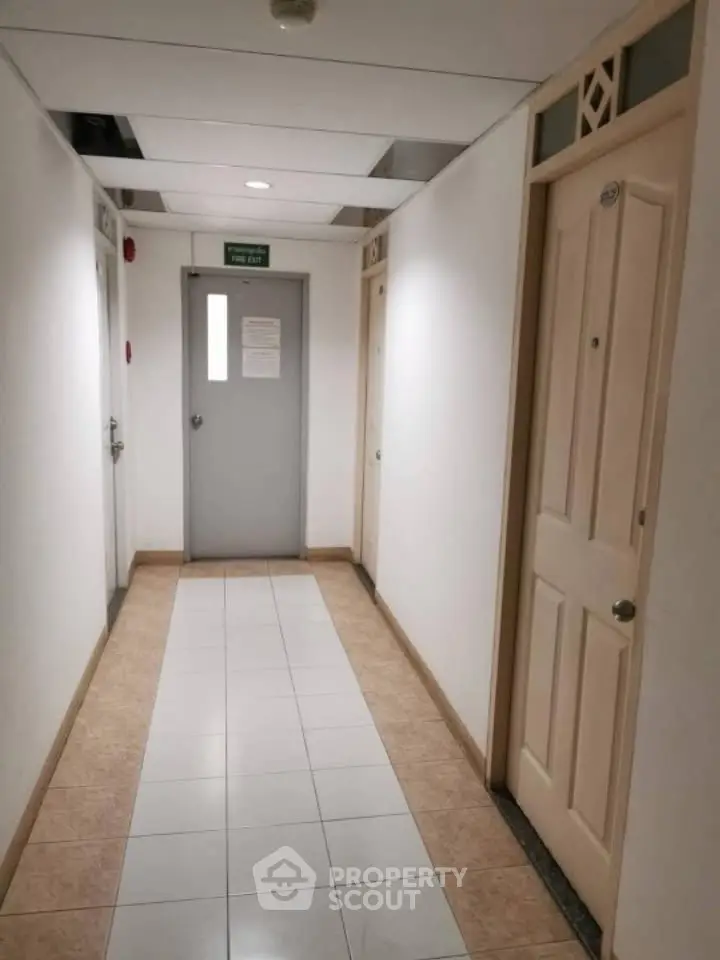 Spacious corridor with multiple doors in a modern building, featuring clean tiled flooring and bright lighting.