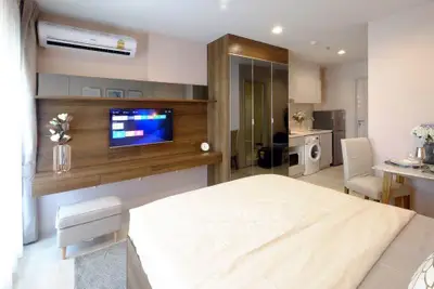 Modern studio apartment with stylish decor, featuring a wall-mounted TV, air conditioning, and in-unit laundry.