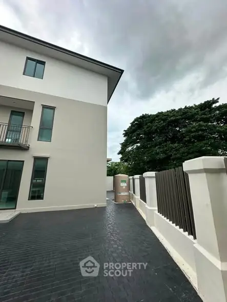 Modern three-story building exterior with sleek design and spacious driveway, surrounded by lush greenery.