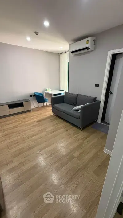 Modern living room with sleek furniture and wooden flooring, featuring a cozy sofa and air conditioning.