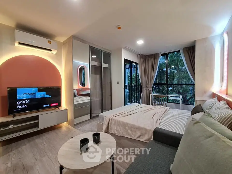 Modern bedroom with large windows and stylish decor, featuring a cozy seating area and a wall-mounted TV.