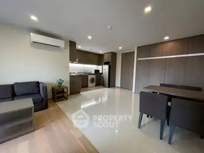 Modern living room with open kitchen and dining area, featuring sleek furniture and appliances.