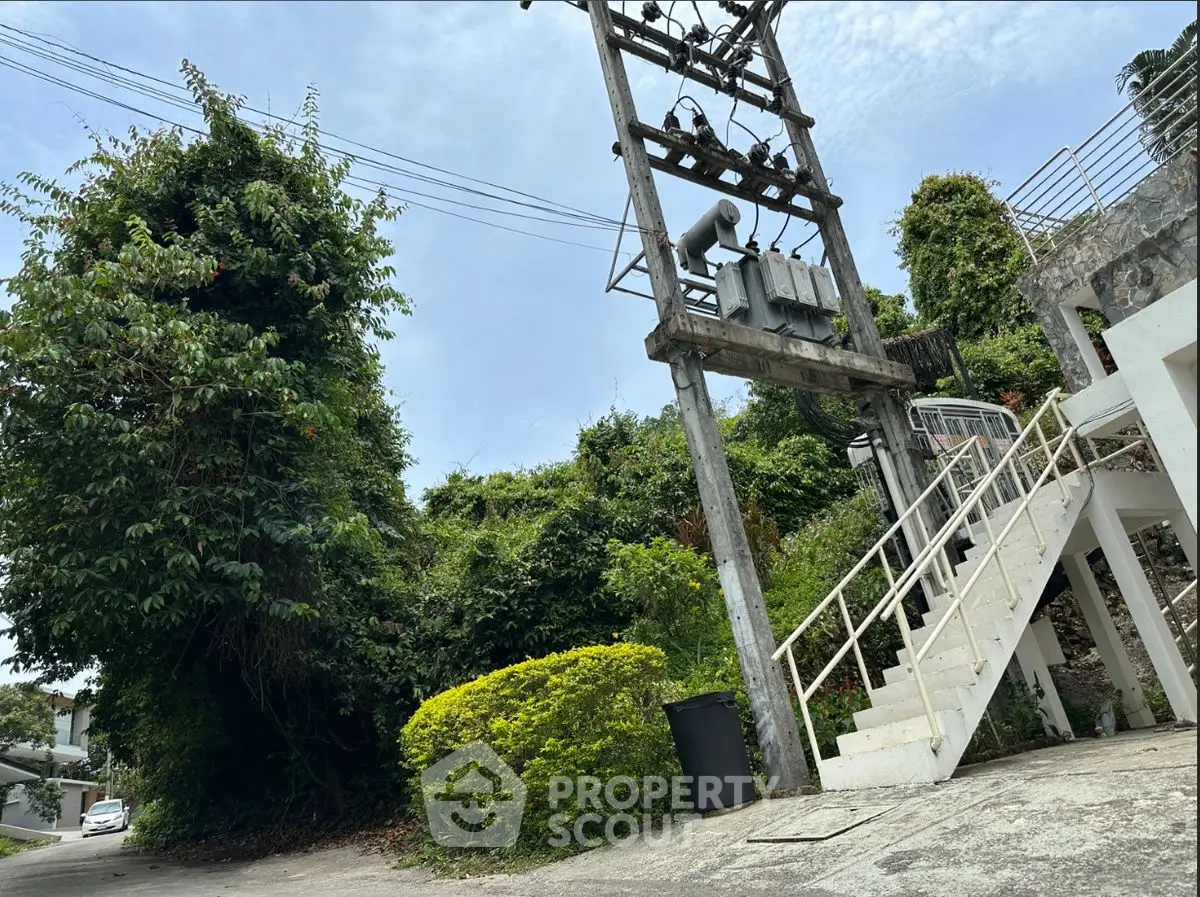 Lush greenery surrounds a residential entrance with stairs and power lines, offering a serene natural setting.