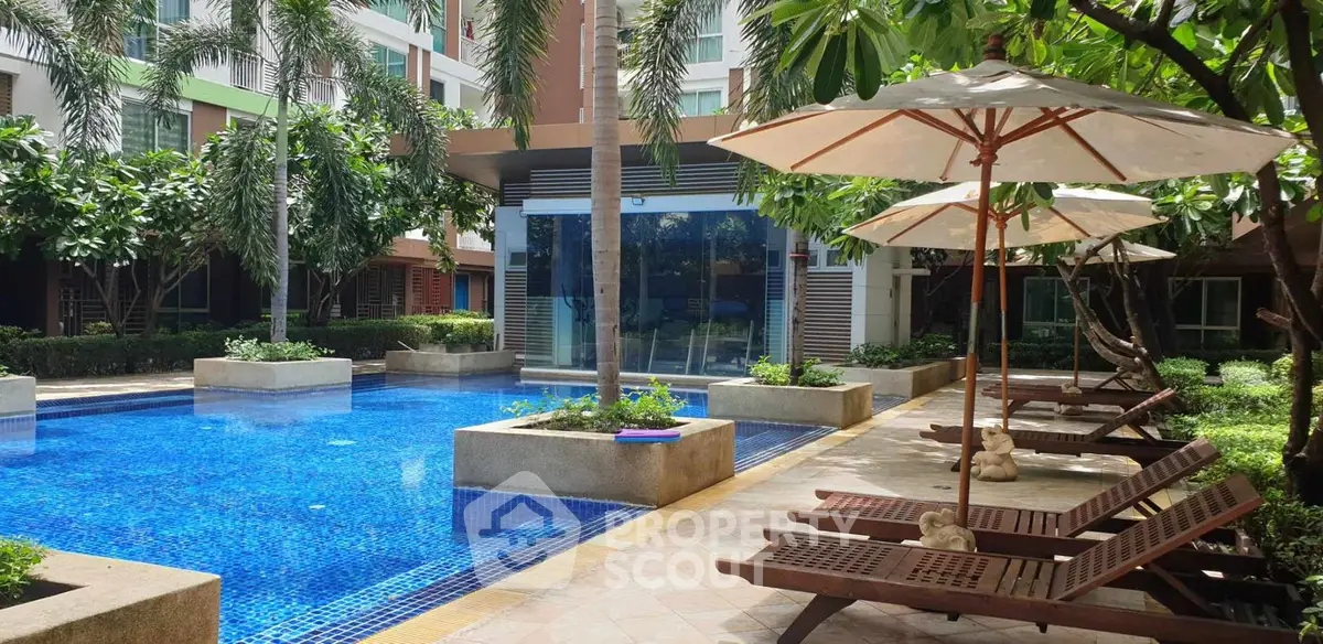 Luxurious outdoor pool area with sun loungers and umbrellas in a modern residential complex.