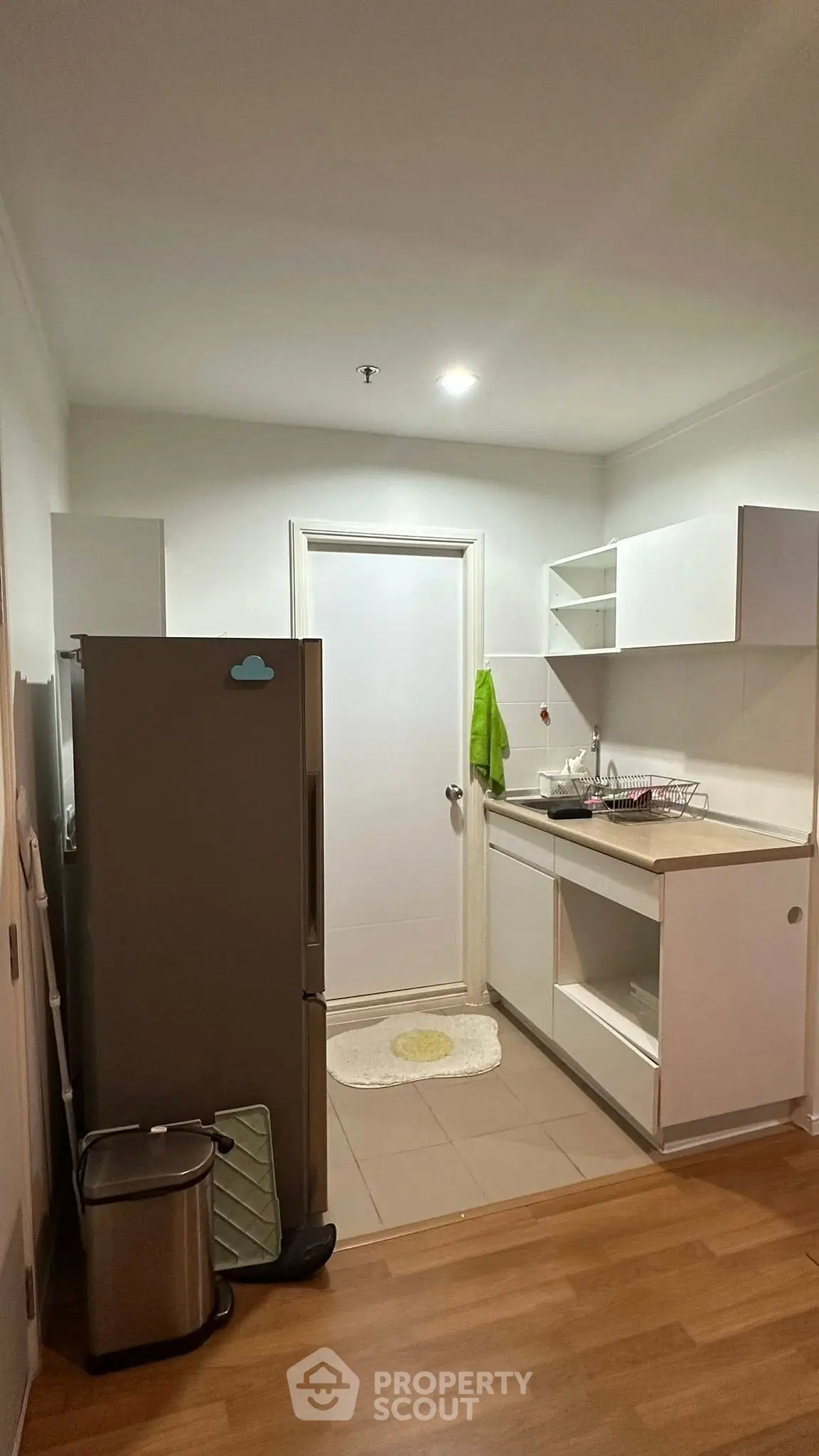 Modern kitchen with sleek white cabinets and stainless steel fridge in cozy apartment.