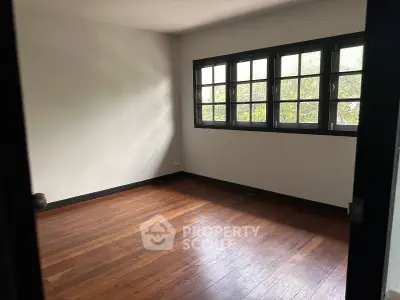 Spacious empty room with wooden floors and large windows offering natural light.