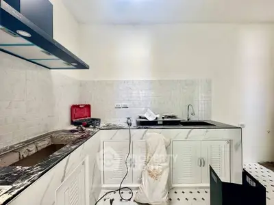 Modern kitchen under renovation with marble countertops and white cabinetry.