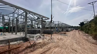 New construction site with steel frames and dirt road under a clear sky.