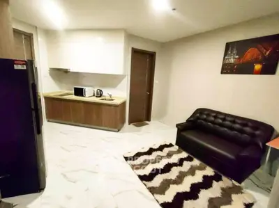 Modern apartment interior with sleek kitchen and cozy living area featuring a stylish black sofa and patterned rug.