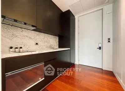 Sleek modern kitchen with dark cabinetry and marble backsplash in luxury apartment.