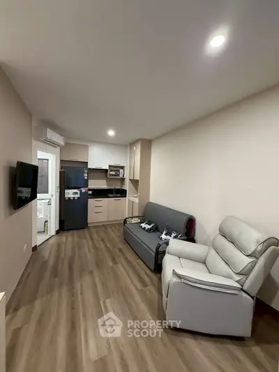 Modern living room with sleek kitchen, cozy seating, and stylish flooring in a compact apartment.