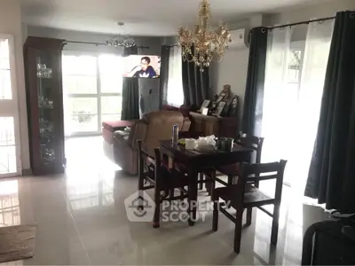 Elegant living room with chandelier and natural light, featuring a cozy dining area and modern furnishings.