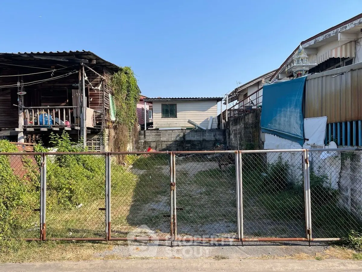 Vacant lot with metal gate and adjacent houses, ideal for new construction.