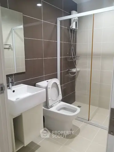 Modern bathroom with neutral tones, featuring a glass shower enclosure, wall-mounted sink, and a white ceramic toilet.