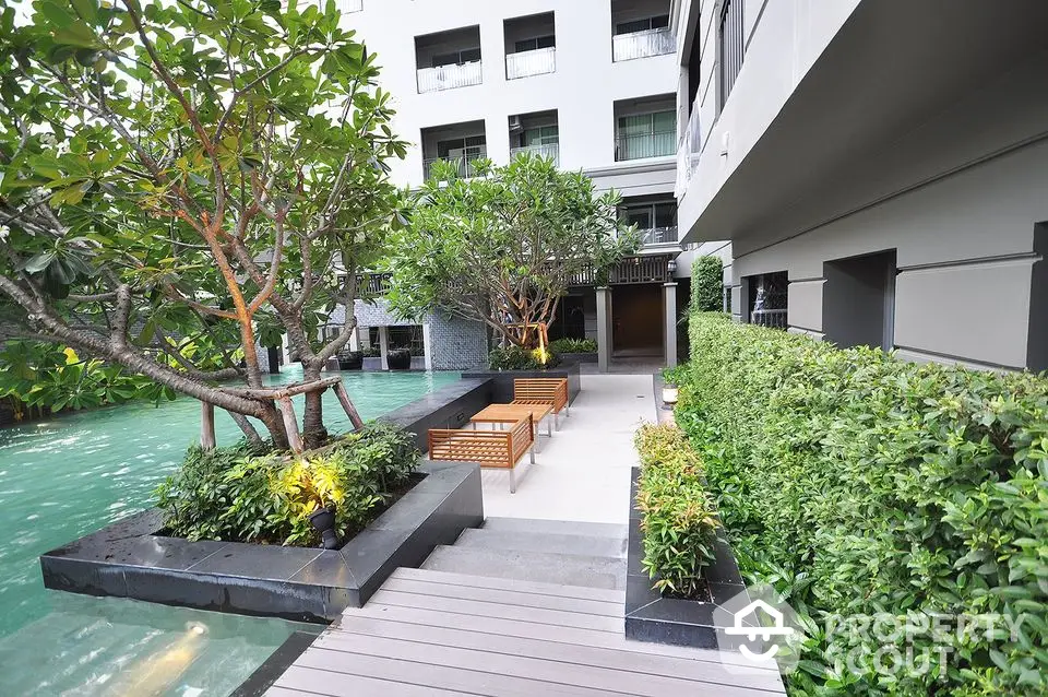 Luxurious apartment complex with serene garden and poolside seating area