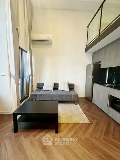 Modern living room with high ceilings and mezzanine, featuring sleek furniture and stylish kitchen.