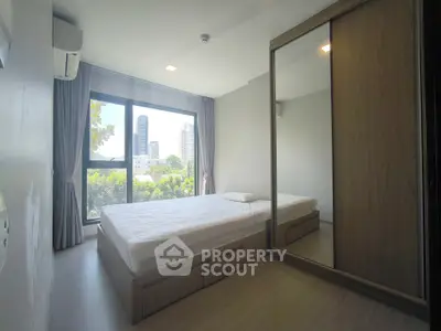 Modern bedroom with large window and mirrored wardrobe, offering city views.