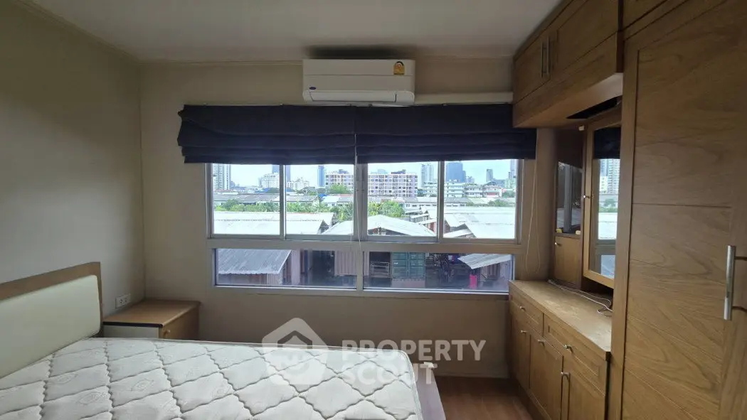 Cozy bedroom with large window offering city view and built-in wooden wardrobe.