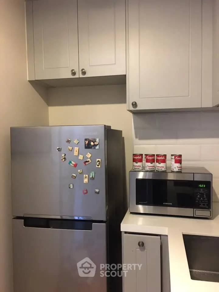Modern kitchen with stainless steel fridge and microwave, sleek cabinetry, and minimalist design.