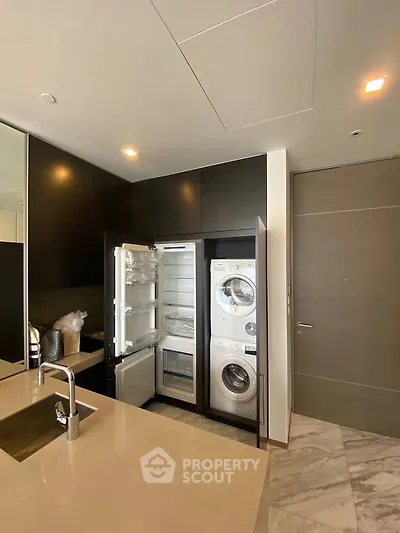 Modern kitchen with integrated appliances including fridge and washer-dryer, sleek cabinetry, and marble flooring.
