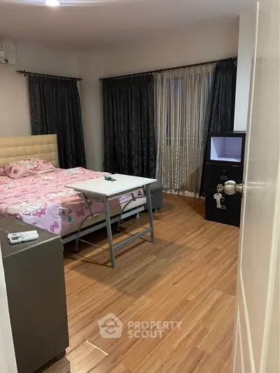 Cozy bedroom with wooden flooring and stylish curtains, featuring a comfortable bed and modern decor.