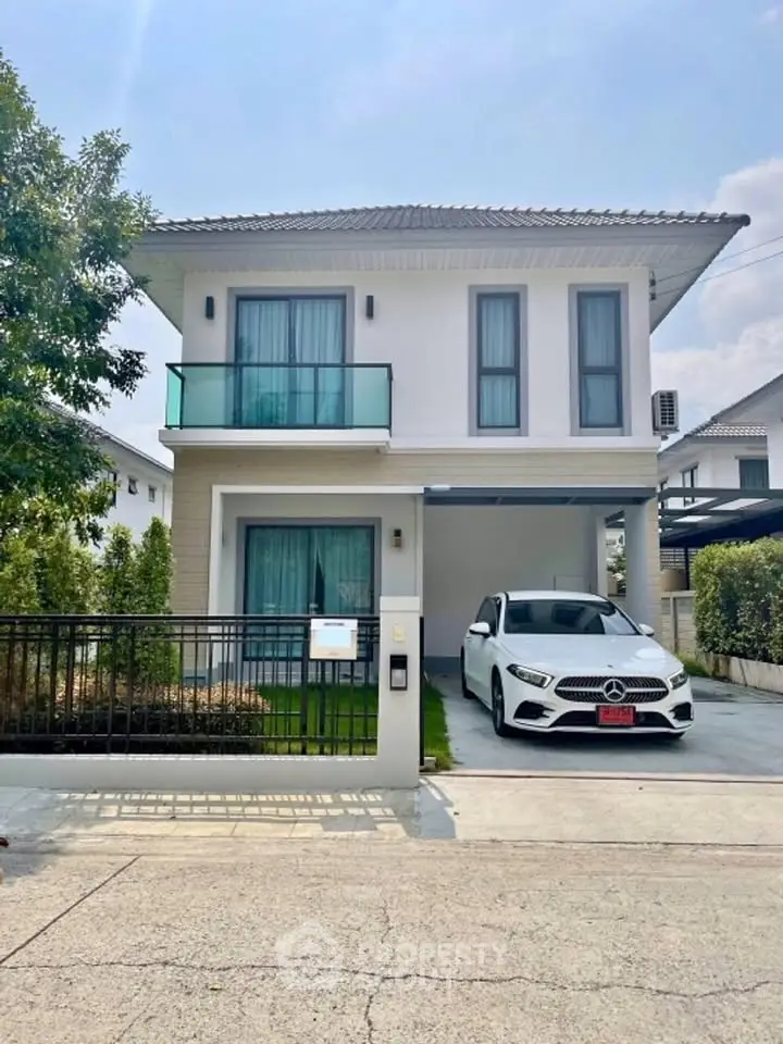 Modern two-story house with a sleek car parked in the driveway, featuring a small balcony and lush greenery.