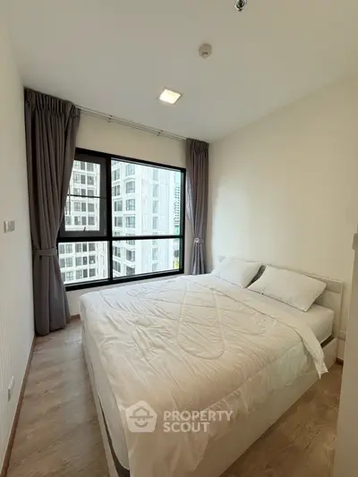 Cozy bedroom with large window and city view in modern apartment