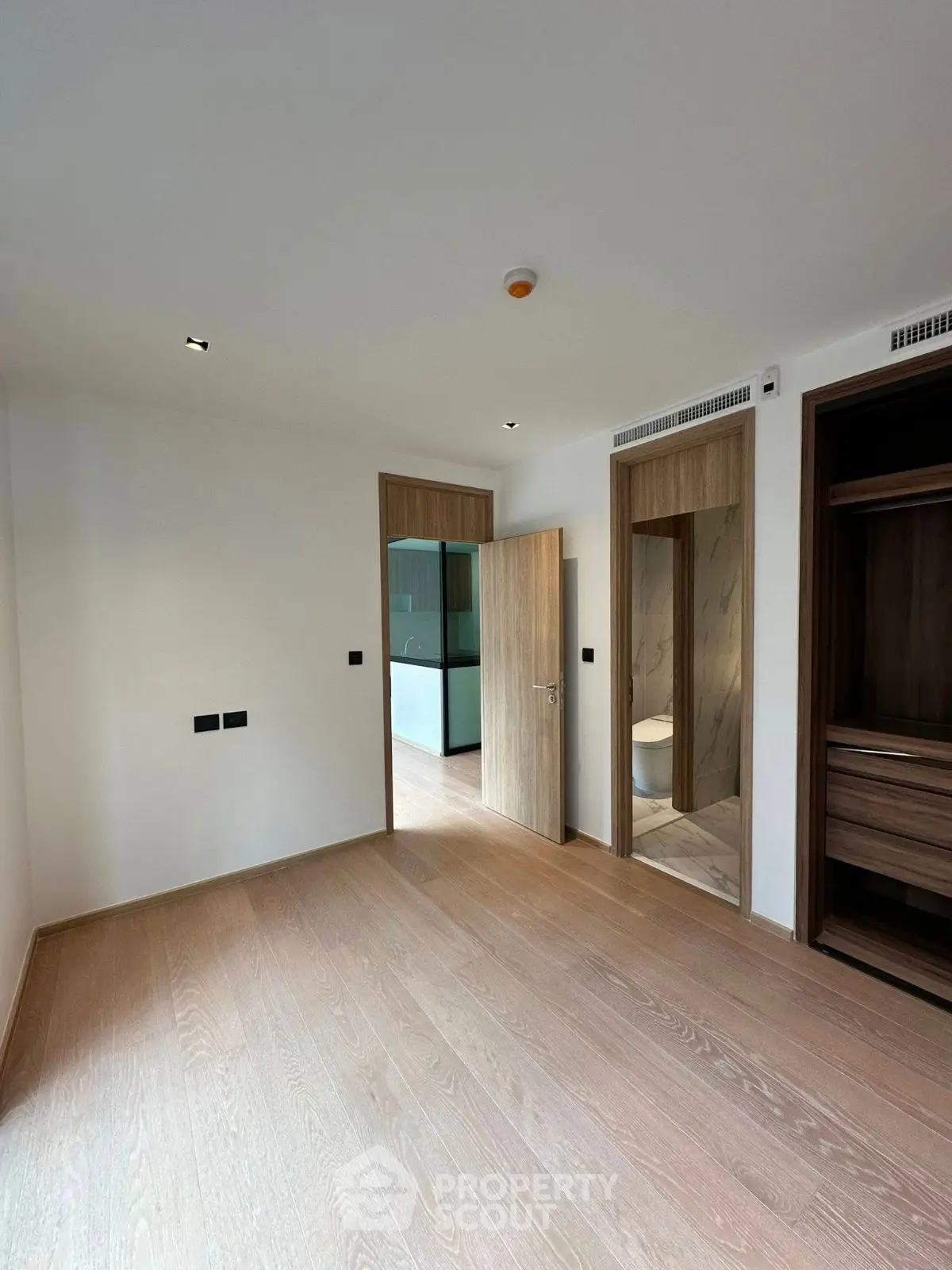 Spacious modern bedroom with wooden flooring and ensuite bathroom in luxury apartment.