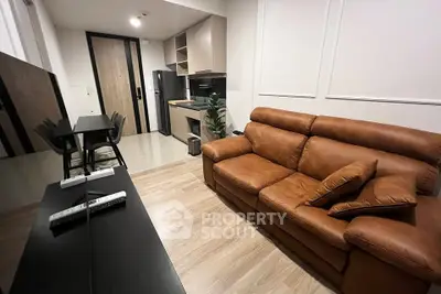 Modern living room with brown leather sofa and sleek kitchen area in open layout apartment.