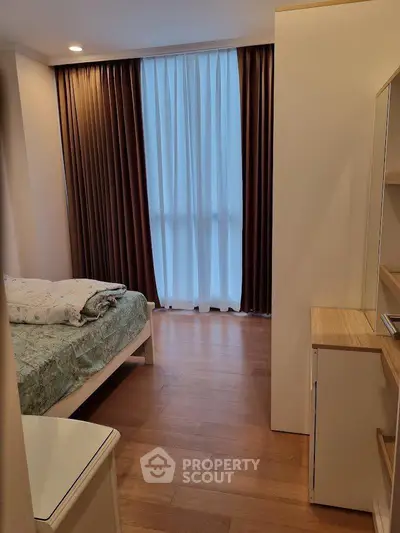 Cozy bedroom with wooden flooring and elegant curtains in modern apartment.