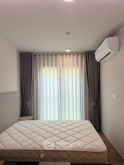 Modern bedroom with natural light and air conditioning, featuring elegant curtains and a comfortable mattress.