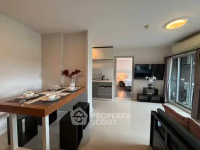 Modern open-plan living room with dining area and view into bedroom, featuring sleek furniture and decor.