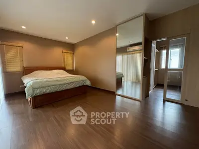 Spacious bedroom with wooden flooring and large mirror, featuring cozy bed and ample natural light.