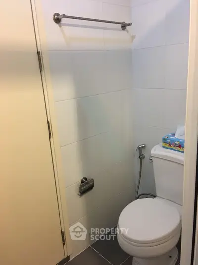 Compact bathroom with white tiles and modern fixtures, featuring a toilet and tissue holder.