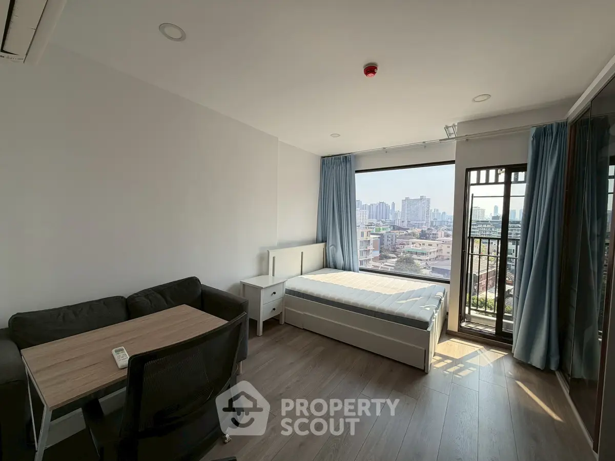 Modern studio apartment with city view, featuring a cozy living area and balcony access.
