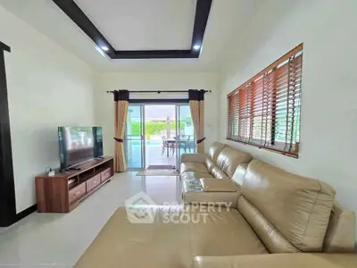 Spacious living room with modern leather sofa and large TV, opening to a bright patio area.