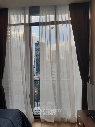 Stunning city view from a modern bedroom with floor-to-ceiling windows and elegant curtains.