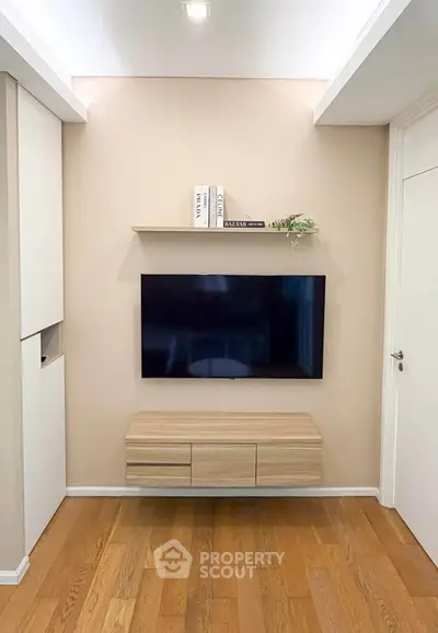Modern living room with wall-mounted TV and wooden flooring, featuring sleek storage solutions.