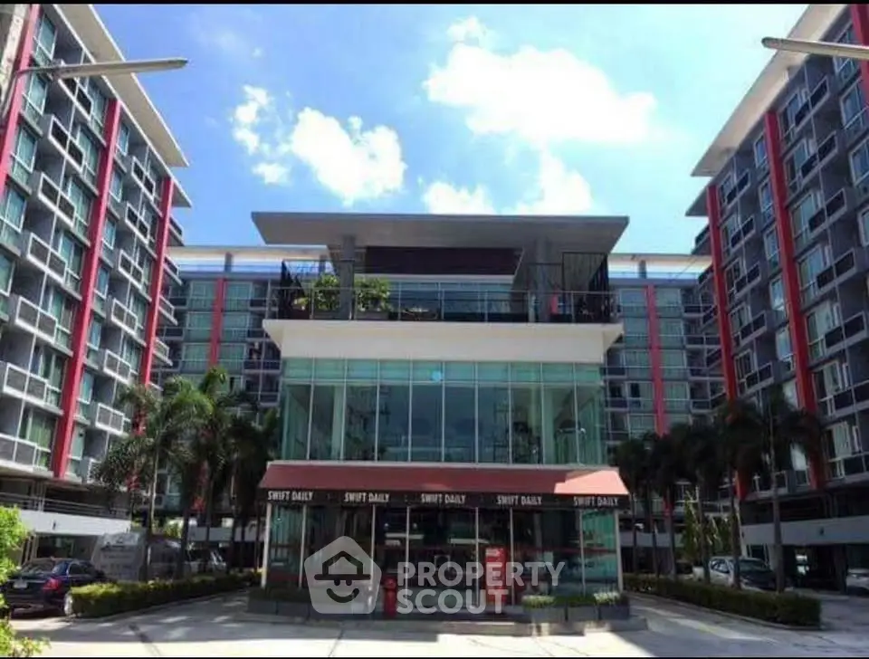 Modern apartment building with glass facade and palm trees under a clear blue sky.