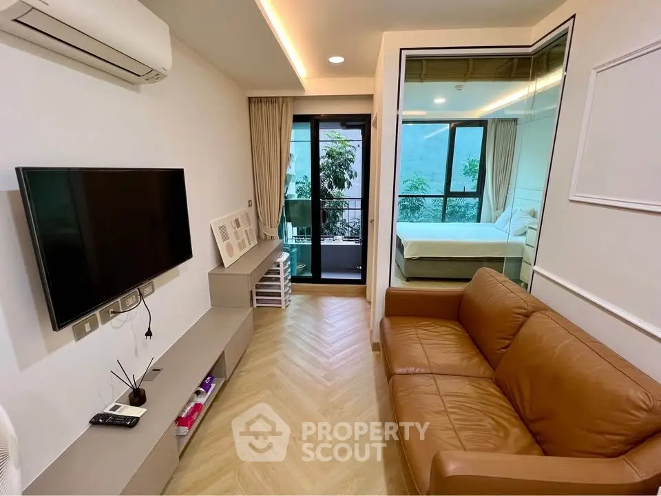 Modern living room with brown leather sofa and large TV, leading to a bedroom with glass partition and balcony view.