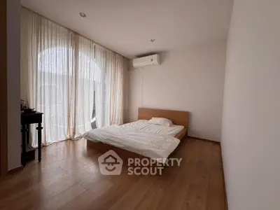 Spacious minimalist bedroom with wooden flooring and large window drapes.