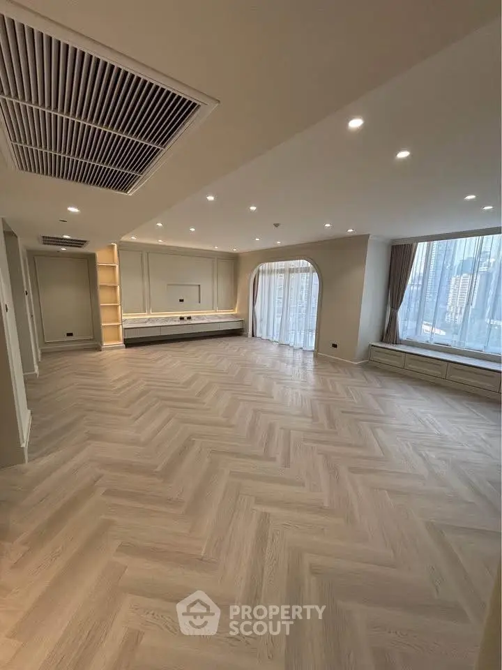 Spacious modern living room with elegant herringbone flooring and large windows.