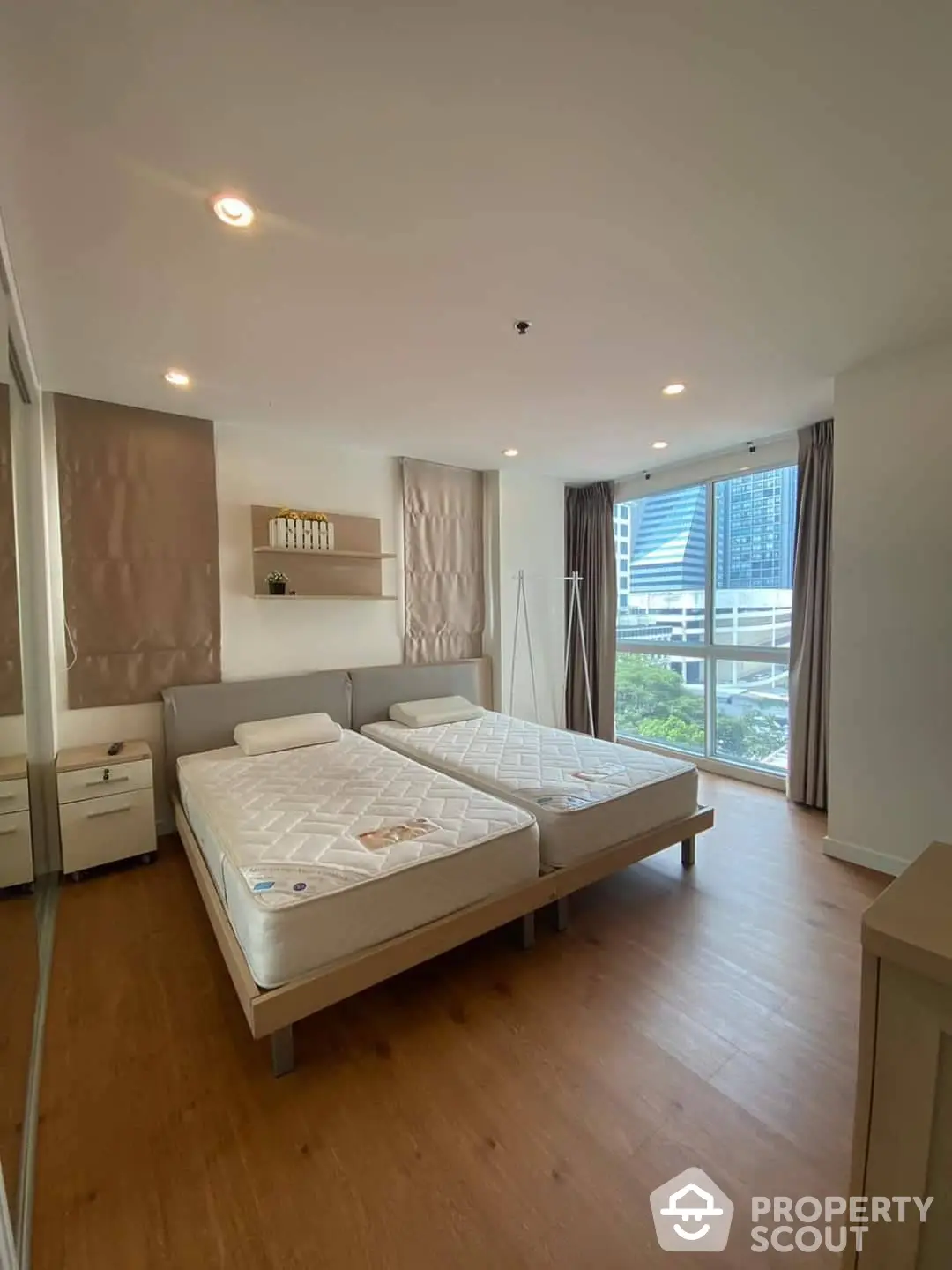 Spacious and well-lit bedroom with two large beds, modern lighting, and a view of the city through floor-to-ceiling windows, complete with elegant furnishings.