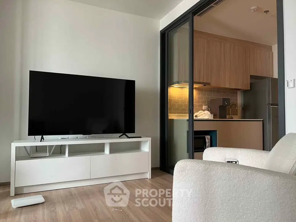 Modern living room with sleek TV setup and open kitchen layout in stylish apartment.