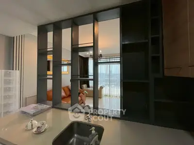 Modern living room with open kitchen and stylish shelving, featuring a cozy sofa and large windows with city views.