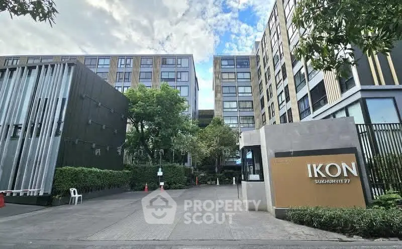 Modern apartment complex entrance with lush greenery and contemporary design.