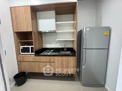 Modern kitchen with sleek wooden cabinets, microwave, and stainless steel fridge in compact layout.
