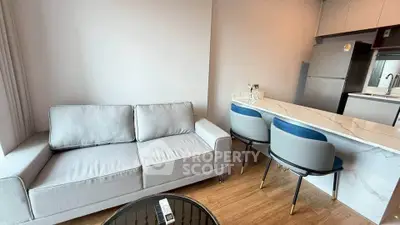 Modern living room with sleek kitchen, featuring cozy sofa and stylish bar stools.