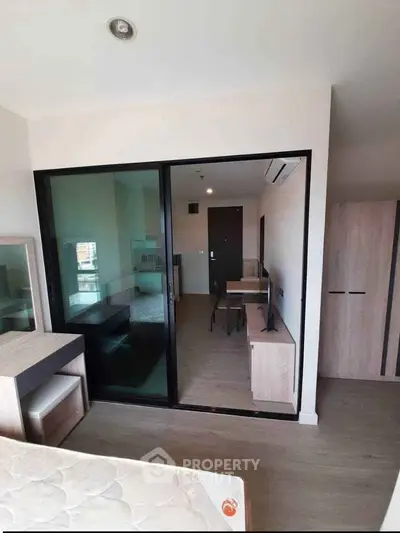 Modern apartment interior with glass partition, wooden flooring, and minimalist furniture design.