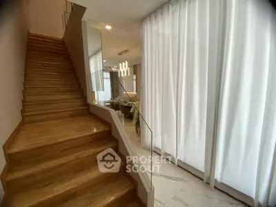 Elegant staircase leading to a modern living area with floor-to-ceiling curtains and stylish lighting.